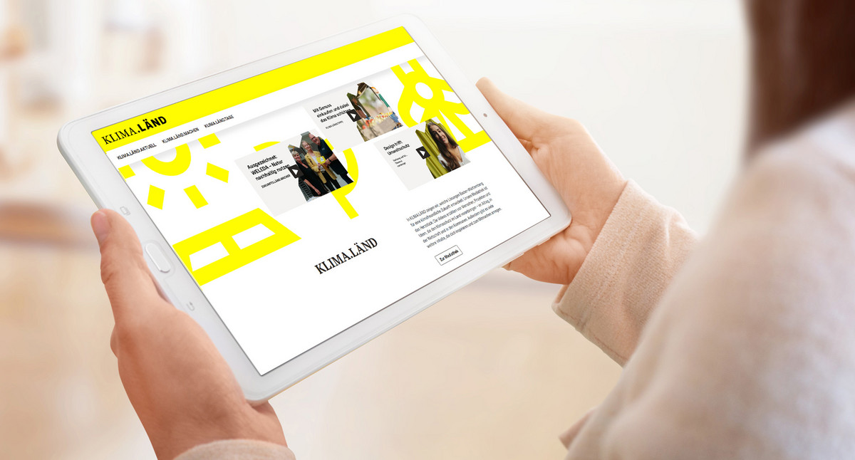 Eine Frau hält ein Tablet, auf dem die Internetseite KLIMA.LÄND geöffnet ist.