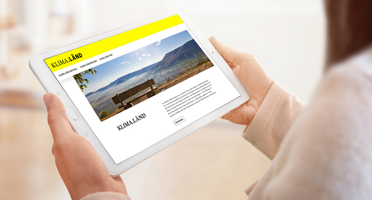 Eine Frau hält ein Tablet, auf dem die Internetseite KLIMA.LÄND geöffnet ist.