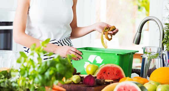 Frau wirft Biomüll von Obst und Gemüse in einen Behälter